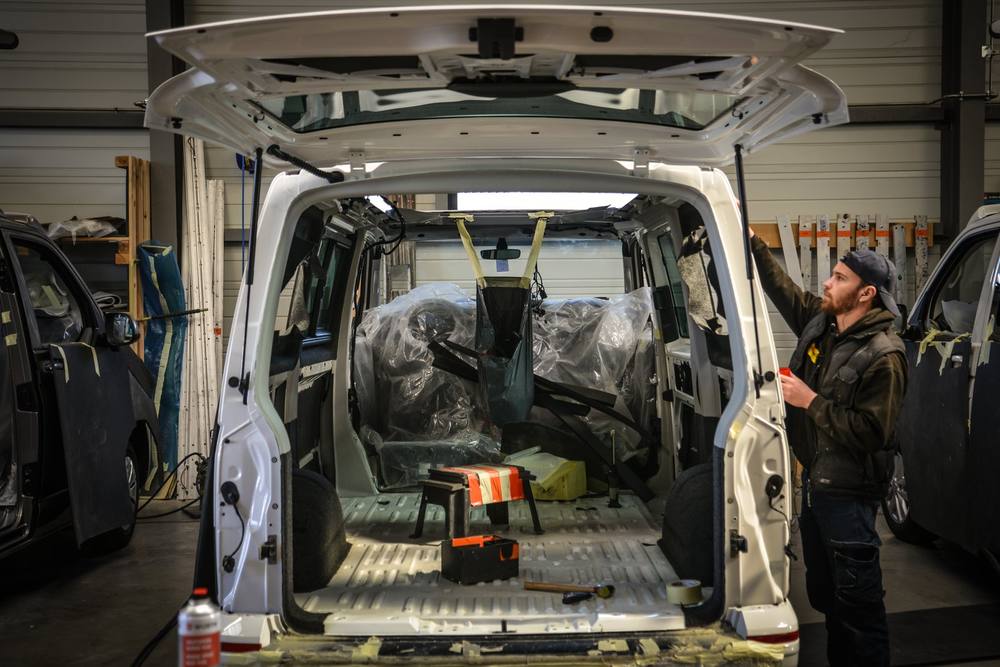 Un van toutes portes ouvertes dans l’atelier, examiné par un technicien Eco Campers