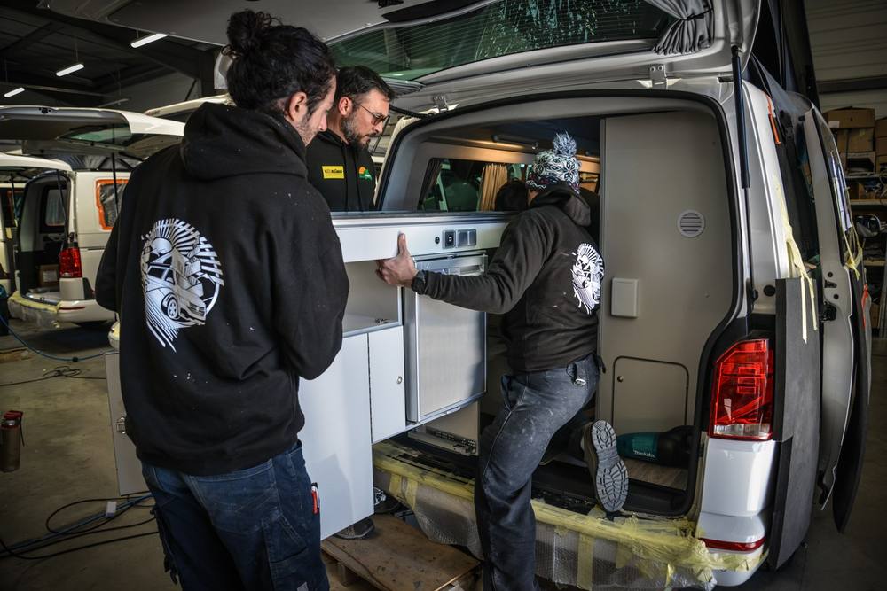 Trois membres de l’équipe Eco Campers engagent un bloc cuisine par le hayon d’un van
