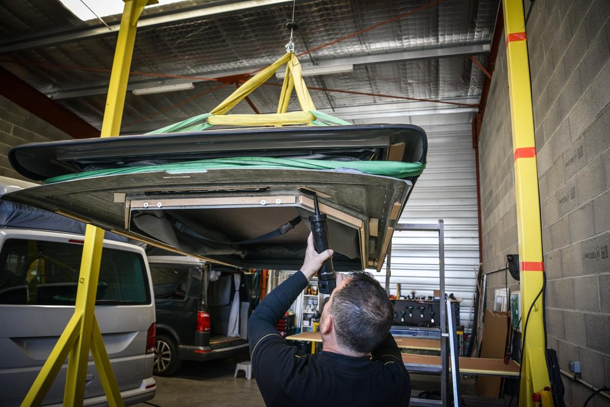Un toit relevable suspendu au palan au-dessus d’un van, dans l’atelier Eco Campers