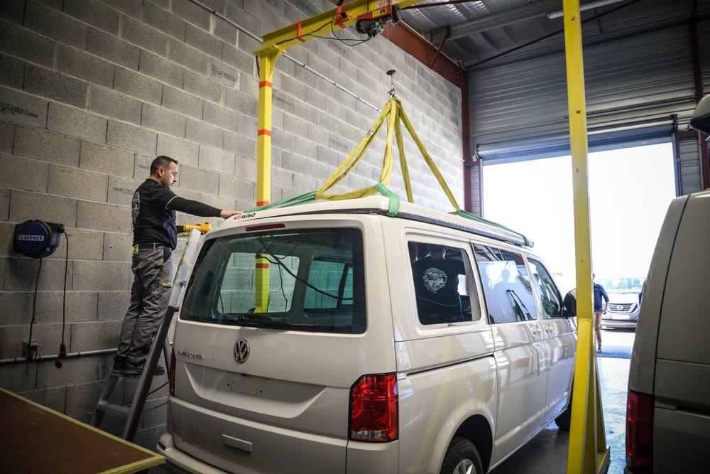 Un technicien Eco Campers intervient sur le toit d’un van, sous le portique de l’atelier